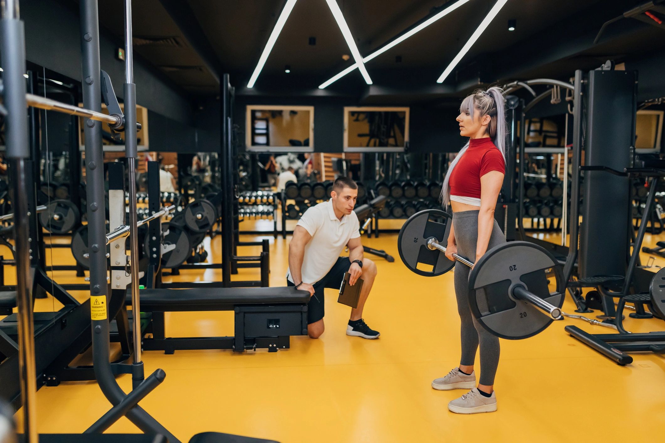 Personal trainer observing a client doing a barbell deadlift